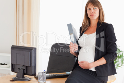 Good looking pregnant female holding a file while standing