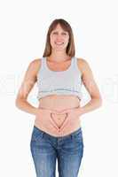 Lovely pregnant female posing while forming a heart with her han