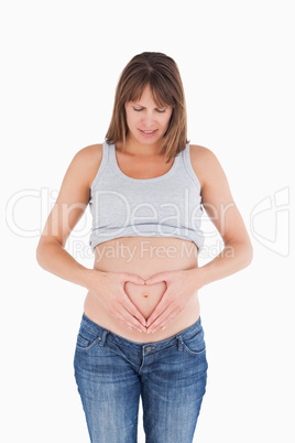 Attractive pregnant female posing while forming a heart with her