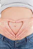 Close-up of a pregnant female posing while forming a heart with