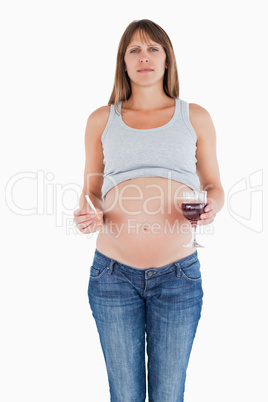 Beautiful pregnant woman holding a glass of red wine while stand
