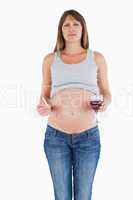 Beautiful pregnant woman holding a glass of red wine while stand