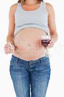 Young pregnant woman holding a glass of red wine while standing
