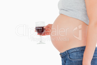 View profile of a pregnant woman holding a glass of red wine whi