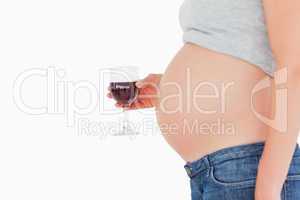 View profile of a pregnant woman holding a glass of red wine whi