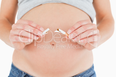 Young pregnant woman holding a broken cigarette while standing