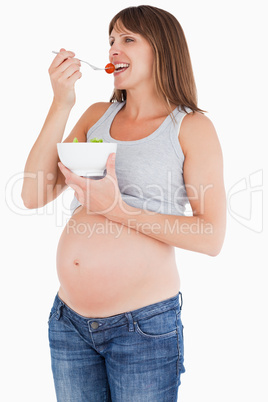 Beautiful pregnant woman eating a cherry tomato while holding a