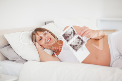 Pretty pregnant woman holding an ultrasound scan while lying on