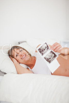 Beautiful pregnant woman holding an ultrasound scan while lying