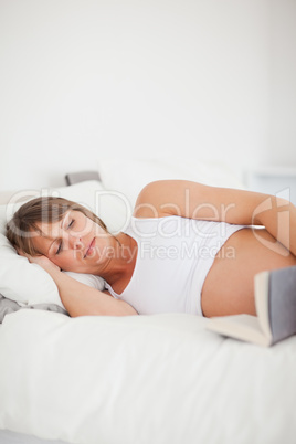 Good looking pregnant woman reading a book while lying on her be