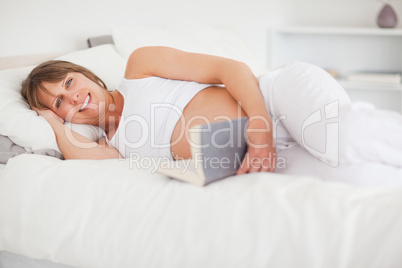 Cute pregnant woman reading a book while lying on her bed