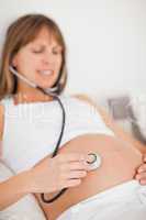 Attractive pregnant woman using a stethoscope while lying on a b