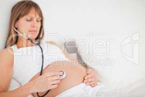 Beautiful pregnant woman using a stethoscope while lying on a be