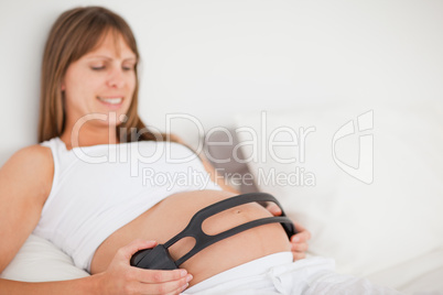 Attractive pregnant woman using headphones while lying on a bed