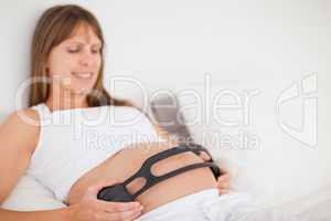 Attractive pregnant woman using headphones while lying on a bed