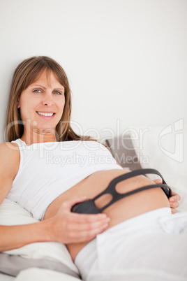 Beautiful pregnant woman using headphones while lying on a bed