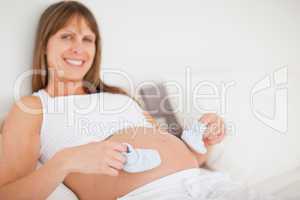 Attractive pregnant woman playing with little socks while lying