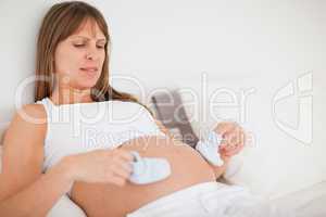 Good looking pregnant woman playing with little socks while lyin