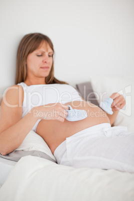 Pretty pregnant woman playing with little socks while lying on a