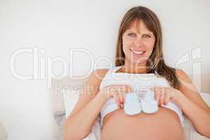 Cute pregnant woman playing with little socks while lying on a b