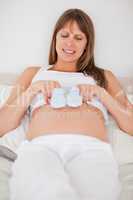 Beautiful pregnant woman playing with little socks while lying o