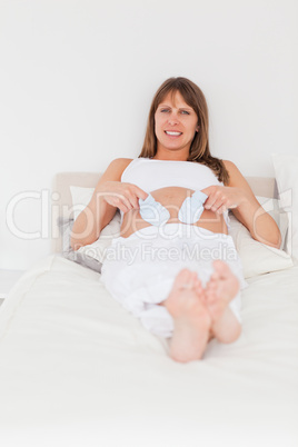 Beautiful pregnant female playing with little socks while lying