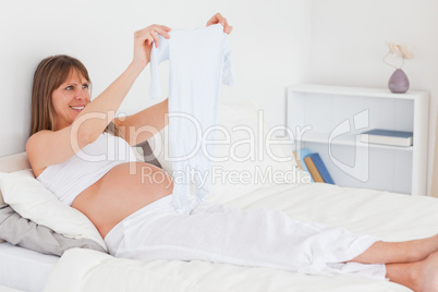 Charming pregnant female showing a little white pyjama while lyi
