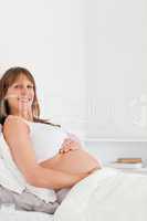 Portrait of a lovely pregnant female posing while lying on a bed