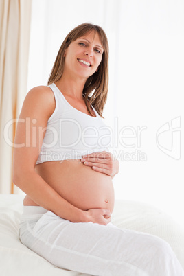Portrait of a lovely pregnant female posing while sitting on a b
