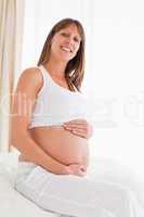 Portrait of a lovely pregnant female posing while sitting on a b