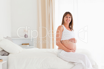 Beautiful pregnant female posing while sitting on a bed