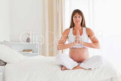 Beautiful pregnant female doing yoga on a bed