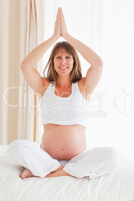 Attractive pregnant female doing yoga on a bed