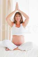 Attractive pregnant female doing yoga on a bed