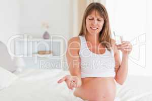 Portrait of a beautiful pregnant female taking a pill while sitt