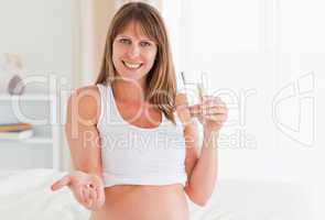 Portrait of an attractive pregnant female taking a pill while si