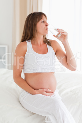 Charming pregnant female taking a pill while sitting on a bed