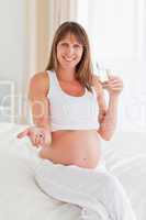 Lovely pregnant female taking a pill while sitting on a bed
