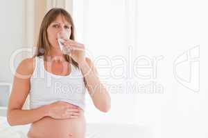 Cute pregnant female taking a pill while sitting on a bed