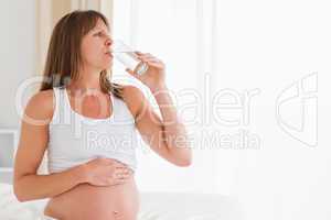 Gorgeous pregnant female taking a pill while sitting on a bed