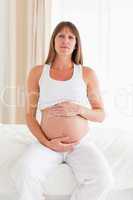 Cute pregnant female caressing her belly while sitting on a bed