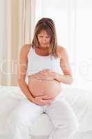 Lovely pregnant female caressing her belly while sitting on a be