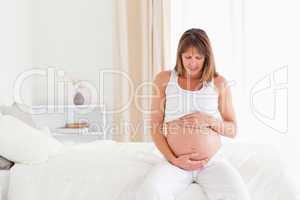 Attractive pregnant female caressing her belly while sitting on