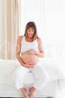 Good looking pregnant female caressing her belly while sitting o