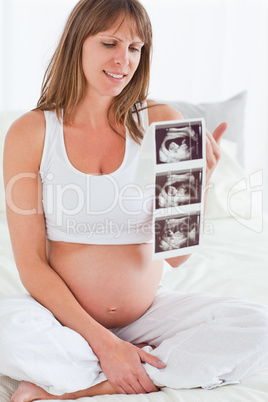 Charming pregnant female showing an ultrasound scan while sittin