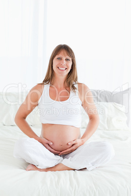 Beautiful pregnant female posing while sitting on a bed