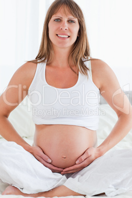 Portrait of a young pregnant female posing while sitting on a be