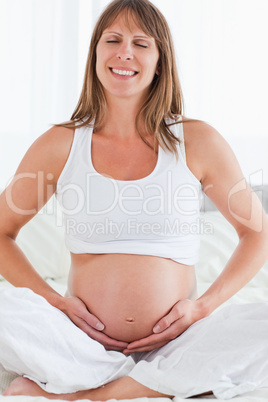 Portrait of a pregnant female posing while sitting on a bed