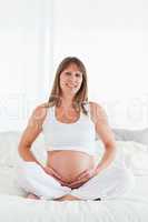 Attractive pregnant female posing while sitting on a bed
