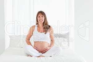 Good looking pregnant female posing while sitting on a bed